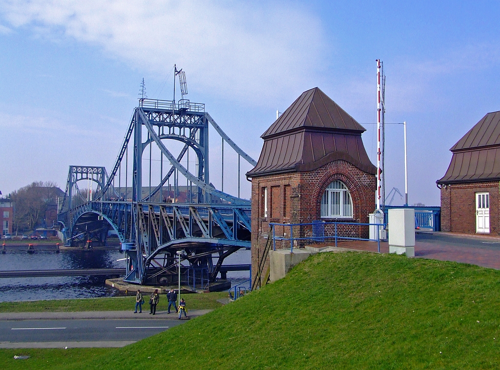 Die Kaiser-Wilhelm-Brcke in Wilhelmshaven am 16.04.2006. Sie ist eine symmetrische, zweiflgelige Straen-Dreh-Brcke aus genietetem Stahlfachwerk und das Wahrzeichen von Wilhelmshaven. Sie hat eine Spannweite von 159 Metern, eine Breite von acht Metern und dient - bis heute - als Verbindung zwischen der Sdstadt und der Sdstrandpromenade. Die Durchfahrtshhe betrgt 9 m, die Durchfahrtsbreite 58 m. Damit ist sie die grte deutsche Drehbrcke geblieben. Die sthlernen Flgel der Kaiser-Wilhelm-Brcke bewegen sich unabhngig voneinander und wurden ursprnglich durch getrennte Fahrstnde in den Brckenhusern gesteuert. Seit 1995 sind sie durch eine Person zentral zu bedienen. 