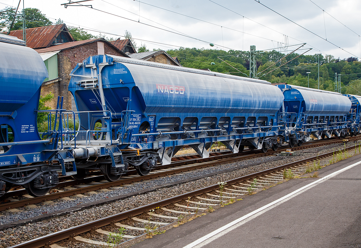 4-achsiger Trichtermittenentladewagen 82,5 m der Gattung Tadns (Drehgestell-Schttgutwagen mit Schwenkdach) beladen mit Kalk, 37 84 0839 008-6 NL- NACCO, der NACCO GmbH, am 07.07.2019 im Zugverbund bei einer Zugdurchfahrt in Betzdorf (Sieg). Seit August 2018 gehren diese Wagen der WASCOSA AG und wurden spter umgezeichnet. 

Der mit einer hohen bilateral kontrollierten Schwerkraftentladung und einem zu ffnenden Dach ausgestattete Wagen ist fr den Transport von Kalksteinen und anderen Schttgtern, die vor Witterungseinflssen geschtzt werden mssen, konzipiert worden. Das Schttgut wird mit Hilfe der Schwerkraft ber die Dachffnung eingefllt. Das kontrollierte Entladen wird manuell durchgefhrt. Die Entleereinrichtung besteht aus 4 Auslauftrichtern die mit je 2 Klappen verschlossen sind und manuell per Hebel, einzeln von den beiden Plattformen an den Wagenenden aus bettigt werden. Die Komplette Entladung des Wagens ist durch ffnung auf nur einer Seite mglich. Die Entladung des Wagens erfolgt auf Frderbndern oder in unterirdische Bunker.

TECHNISCHE DATEN:
Hersteller: Astra Rail Industries (Rumnien) gehrt zu Greenbrier Europe
Spurweite: 1.435 mm
Ladeprofil: G1-TSI
Lnge ber Puffer : 19.040 mm
Drehzapfenabstand: 14.000 mm
Achsabstand im Drehgestell: 1.800 mm
Eigengewicht: 24.680 kg
Hchstgeschwindigkeit: 100 km/h (beladen) / 120 km/h (leer)
Maximales Ladegewicht: 65,3 t (ab Streckenklasse D)
Kleinster bef. Gleisbogenradius: 75 m
Rauminhalt: 82,5 m
Ladeffnung: 15.080 x 1.200 mm
Dach: Spritzwasserfestes Hub-/Schwenkdach mit Handbettigung
Drehgestell-Typ: Y25Lsd-KP1
Laufraddurchmesser: 920 mm (neu)
Bremse: KE-GP-A (K) max. 58 t
Bremssohle: C 810
Intern. Verwendungsfhigkeit: TEN GE 
Heimatbahnhof: Maschen Rbf

Ein paar Worte zu ehemals NACCO:
Die VTG AG in Hamburg hatte die CIT Rail Holdings (Europe) SAS, der Eigentmerin der NACCO-Gruppe im Mrz 2018 bernommen. Die zustndigen Kartellbehrden hatten der VTG AG den Erwerb unter der Auflage genehmigt, dass rund 30 Prozent des Gterwagenbestands an einen Dritten zu veruern sind.

Die Schweizer Wagenvermieterin Wascosa AG hat rund 4.400 Gterwagen von NACCO/CIT und somit und 30 Prozent der Gterwagenflotte der NACCO-Gruppe bernommen. Nebst dem operativen Geschft und den Wagenmietvertrgen hat Wascosa auch die Mitarbeiter der NACCO GmbH in Hamburg bernommen. Mit der bernahme der rund 4.400 Gterwagen ist die Flotte von Wascosa auf ber 14.000 Gterwagen angewachsen.Damit rckt das Unternehmen hinter VTG, Ermewa und GATX an die vierte Stelle der europischen Wagenvermieter.