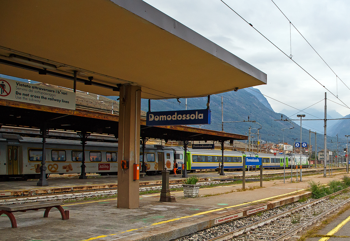 Auf besonderen Wunsch, leider mit vielen Masten über die Bahnsteige hinweg....
Die BLS Werbelok Re 465 008-1  Allegra  (ex Niederhorn) mit Werbung Patenschaft für Berggemeinden steht am 08.09.2021, mit einem EW III Zug u.a. mit dem 1.Klasse Kambly-Wagen. A 50 85 18-34 002-3 CH-BLS, im Bahnhof Domodossola zur Abfahrt nach Brig bereit.
