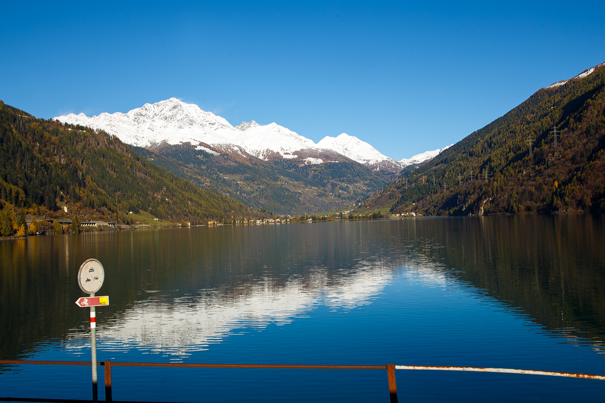 
Aus dem Zug heraus am 04.11.2019 in Miralago (deutsch: Seeblick) im Puschlav ein Seeblick über den Lago di Poschiavo hinweg auf die Berninagruppe. Die höchste Bergspitze ist der mit 4.049 m ü. M. hohe Piz Bernina, der einzige Viertausender der Ostalpen.

Hier links am westlichen Ufer des Sees entlang führt, auf einer Länge von 2 km, die in die Liste des UNESCO-Weltkulturerbes aufgenommen Berninabahn.
