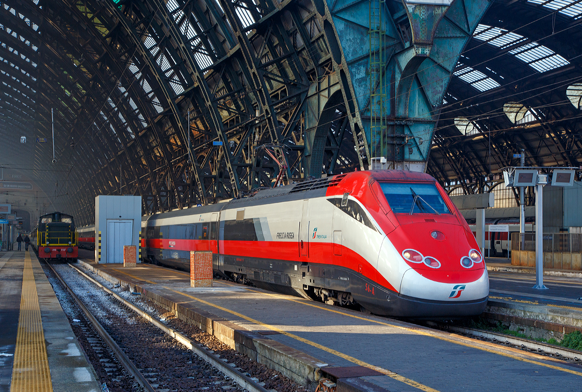 Ausfahrt eines sehr langen  Frecciarossa  (deutsch: roter Pfeil) der Trenitalia (100-prozentige Tochtergesellschaft der Ferrovie dello Stato) am 29.12.2015 vom Bahnhof Milano Centrale (Mailand Zentral). Der Frecciarossa ist eine Zuggattung für Züge mit einer Höchstgeschwindigkeit von 300 km/h. Hier ist es der ETR 500 - 56 ein ETR 500 der 2.Serie. ETR steht ElettroTreno Rapido.

Diese Züge bestehen aus zwei Triebköpfen vom Typ E.404B und aus zwölf Mittelwagen, ETR 500.31 bis 60 komplett der 2.Serie. Bei den ETR 500.01 bis 30 sind nur die beiden Triebköpfe aus der 2.Serie, die Mittelwagen dagegen stammen aus der 1.Serie der ETR 500 (Mono). 

Durch die begrenzte Stromstärke des Gleichstromnetzes können die Hochgeschwindigkeitszüge nur für Geschwindigkeiten bis zu 250 km/h ausreichend mit Energie versorgt werden. Deshalb entschied sich die italienische Staatsbahn in den 1990er Jahren, weitere Neubau-Schnellfahrstrecken mit Wechselstrom (25 kV, 50 Hz) zu betreiben.

Da die erste Serie der ETR 500 nur für das Gleichstromnetz geeignet ist, wurde ab 1996 eine zweite Serie ETR 500 bestellt und geliefert, die sowohl im Gleichstrom- als auch im Wechselstromnetz fahren kann. Die Zweisystem-Fahrzeuge werden Politensione (deutsch: Mehr-Spannung) genannt. Es gab auch mal zwischenzeitlich Dreisystem-Fahrzeuge (ETR 500 F), die auch unter 1.5 kV DC fahren konnten, diese wurden aber wieder zurückgebaut. Diese waren für den Verkehr nach Frankreich gedacht, bekamen aber dort keine Zulassung.

Die zulässige Höchstgeschwindigkeit der ETR 500 der zweiten Serie von 300 km/h wird im regulären Betrieb aber nur mit Wechselstrom auf neueren Schnellfahrstrecken Italiens erreicht.

Im Gegensatz zur ersten Serie werden bei der zweiten Serie Einholmstromabnehmer verwendet. Die Triebköpfe verfügen jeweils über einen Abnehmer für Gleichstrom und einen Abnehmer für Wechselstrom. Äußerlich unterscheiden sich die beiden Bauserien durch starke Unterschiede des „Gesichts“. Die Front der zweiten Serie wurde aufgelockert und rundlicher gestaltet, besonders betont durch die getrennt angeordneten Spitzensignale, während die Frontscheiben kleiner und rechteckig ausgeführt wurden. Wobei ja die Triebköpfe (E.404A) der ersten Serie zu Lokomotiven der Baureihe E.414 umgebaut wurden.


TECHNISCHE DATEN:
Von einem Triebkopf E.404B
Spurweite:  1.435 mm (Normalspur)
Achsformel: Bo'Bo'
Länge: 20.250 mm
Höhe: 4.000 mm
Breite: 3.020 mm
Drehzapfenabstand:  11.450 mm
Achsabstand im Drehgestell: 3.000 mm
Dienstgewicht: 68 t
Höchstgeschwindigkeit: 300 km/h
Dauerleistung: 4.400 kW (4 x 1.100 kW) pro Triebkopf
Treibraddurchmesser:  1.100 mm
Stromsysteme: 3000 V DC und 25 kV 50 Hz AC

Daten der Mittelwagen:
Länge: 26.100 mm
Drehzapfenabstand:  19.000 mm
Achsabstand im Drehgestell: 3.000 mm
Eigengewicht: 40 t

Gesamtzug Daten:
Achsformel: Bo'Bo' (12x 2'2') Bo'Bo'
Gesamtzuglänge: 353.700 mm (bei 12 Mittelwagen)
Gesamteigengewicht: 616 t
Dauerleistung: 8.800 kW
Anfahrzugkraft:  400 kN