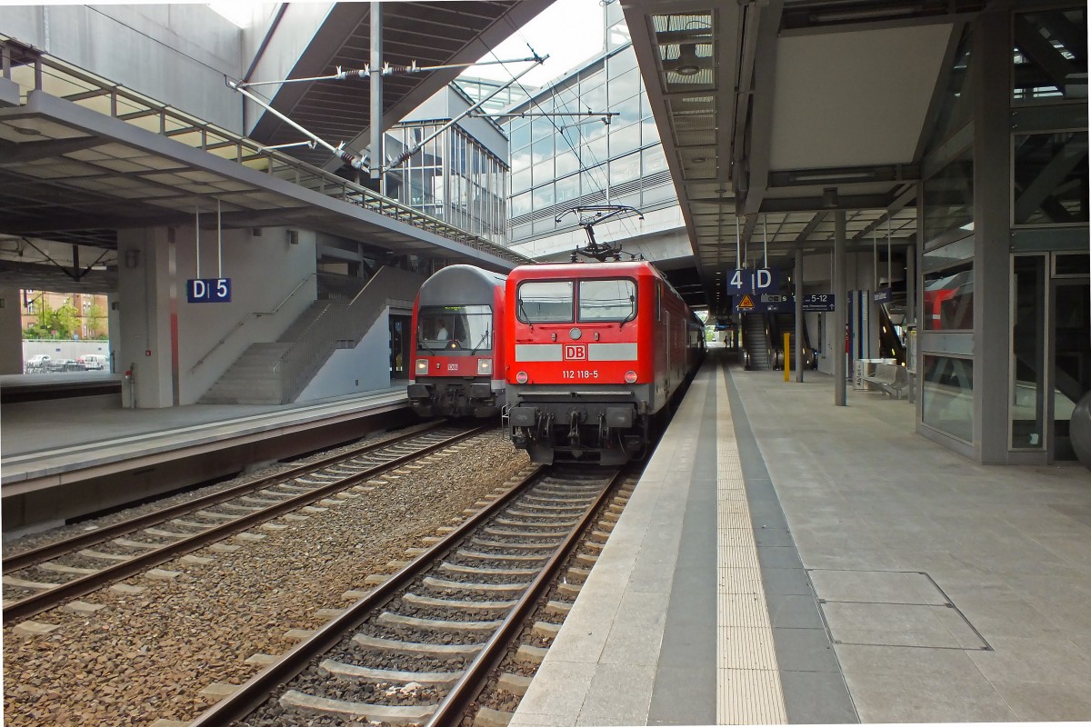 Beton, Glas und unübersichtliche Wege, die großenteils wohl zu einem nie realisierten Parkdeck gehören und nicht genutzt werden, wie besipielsweise die Treppe links neben dem Steuerwagen kennzeichnen den Bahnhof Berlin Südkreuz. 112 118 ist mit einem RE5 auf dem Weg nach Lutherstadt Wittenberg, während der mit einer giftgrünen Matrixanzeige ausgerüstete Steuerwagen links zu einem RE3 nach Schwedt (Oder) gehört.