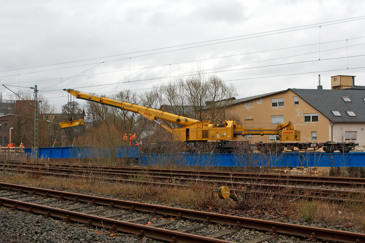 
Der KSW Bahnhof Siegen-Eintracht (Betriebsbereich Eisern-Siegener Eisenbahn), ist von den DB Gleisen (der Siegstrecke KBS 460) durch die Sieg getrennt. Am Bahnhof Siegen-Eintracht befindet sich auch der Hauptsitz der KSW mit Werkstätten, zudem auch die neue Werkstatt der HLB. So ist die eingleisige Siegbrücke die Nabelschnur der KSW Kreisbahn Siegen-Wittgenstein GmbH (KSW) zwischen dem Bahnhof Eintracht und dem Hauptbahnhof Siegen. Die bisherige Brücke war in ihrem Ursprung über 130 Jahre alt und wurde zuletzt 1982 instand gesetzt, aber auf Grund des Alters war ihre Standfestigkeit nicht mehr gewährleistet. Deshalb war auch die maximal erlaubte Geschwindigkeit nur noch Schritttempo. Nun erfolgte der Neubau der Brücke und Auflager, wobei die vorhanden zwei Betonpfeiler überarbeitet wurden. Die Konstruktion ist ein offenes, gekrümmtes Trägerrost in Stahlbauweise mit direkter Schienenbefestigung auf den Längsträgern und damit der bisherigen Brücke sehr ähnlich. Die Kosten für die Sanierung der Siegbrücke belaufen sich auf schätzungsweise rund 1,6 Mio. €, die Hälfte davon trägt der Bund.

So wurde am 20.12.2014 der Brückenoberbau mit Hilfe von dem 150 t Kirow Gleis- und Weichenbaukran KRC 1200+ (ein Kirow MULTI TASKER KRC 1200+) 99 80 9419 005-0 D-STRA  „DONAU“  (ex 97 82 55 508 17-5) der STRABAG RAIL GmbH gesetzt. Der Kran ist hier gekoppelt mit dem Gegenlastwagen 99 80 9 320 001-7 D-STRA. Durch die Lastablegung (Gegengewicht) auf Gegengewichtswagen im Kranbetrieb erfolgt eine Achslastreduzierung.

TECHNISCHE DATEN von dem Kran:
Spurweite: 1.435 mm
Eigengewicht  (in Transportstellung) : 111,0 t 
Länge über Puffer:  15.000 mm  (+13.000 mm Gegenlastwagen)
Motorleistung:  254 kW bei 2.200 U/min
max. Geschwindigkeit im Zugverband: 100 km/h
max. Geschwindigkeit im Eigenantrieb: 19 km/h
Achsanzahl:  8 (in 4 Drehgestelle bzw. 2 Doppeldrehgestelle)
Drehzapfenabstand: 10.000 mm
Drehzapfenabstand im Drehgestell 1 und 2: 2.300 mm
Achsabstand in den Einzeldrehgestellen: 1.100mm
Ergebene Achsabstände in m: 1,1 / 1,2 / 1,1/ 6,6 / 1,1 / 1,2 / 1,1
Achsfolge: 1'A'1A'A1'A1'
Radsatzlast Transport Kran: max. 13,8 t
Radsatzlast Gegengewichtswagen:  max. 20,0 t
Höhe in Transportstellung:  4.300 mm
Breite in Transportstellung:  3.100 mm
max. Ausladung vor Puffer:  21.000 mm
max. Traglast bei max. Ausladung:  40 t
Größte mögliche Traglast: 150 t (abgestützt)  / 120t (freistehend)
max. Hakenhöhe:  24.000 mm
hintere Ausladung (Gegenwicht):  7,9 m–13,5 m
Zul. Anhängelast: 160 t
Kleinster befahrbarer Radius: 80 m (120 m im Schleppbetrieb)


Besondere Ausstattung:
Überhöhenausgleich 180 mm
Schwenkradius ± 360º
Abstützung teleskopierbar bis 8 m Abstützbasis
profilfreies Arbeiten bis ± 30º

Der Kran wurde 2009 von Kirow in Leipzig unter der Fabriknummer 152500 gebaut. Er wird als Schweres Nebenfahrzeug Nr.: 99 80 9419 005-0 (ehemals 97 82 55 508 17-5) geführt und hat die EBA-Nr. EBA 09C02A001. 
