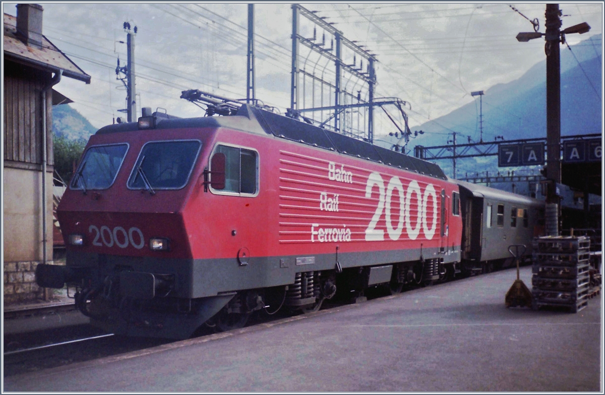 Eine SBB Re 4/4 IV mit einem Schnellzug Richtung Bern (auf dem Bild ist davon nur ein verdeckter Postwagen zu sehen) in Brig.
März 1983
