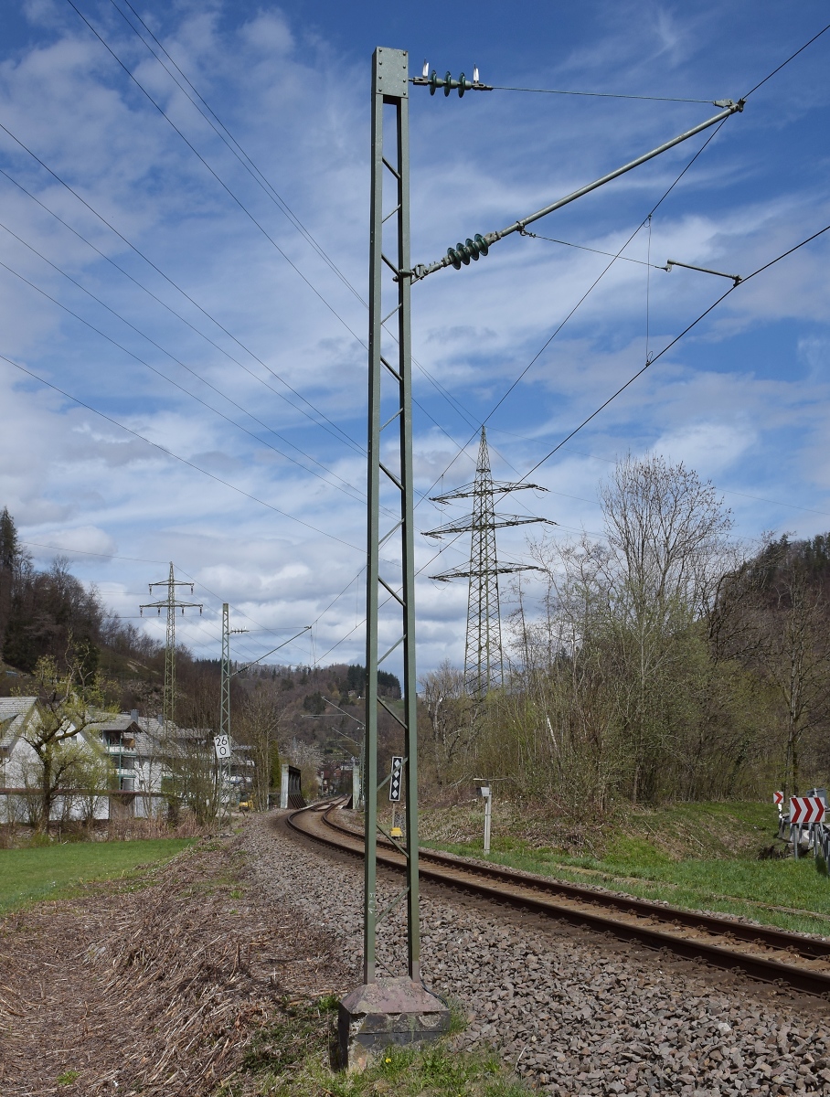 Genauer betrachtet. Noch wenige Originalmasten der badischen Staatsbahn stehen. 1913 wurde hier im Wiesental, an ein paar Lokalbahnen in Bayern, in Preußen und in der Schweiz das 15 kV 16 2/3 Hertz-Stromsystem eingeführt. Womöglich sind diese Masten die letzten, die aus dieser Epoche noch in Betrieb sind. Dahinter steht ein Reichsbahnmast. Die Verstrebung der beiden U-Profile ist beim badischen Mast deutlich filigraner. Zell im Wiesental, April 2021.