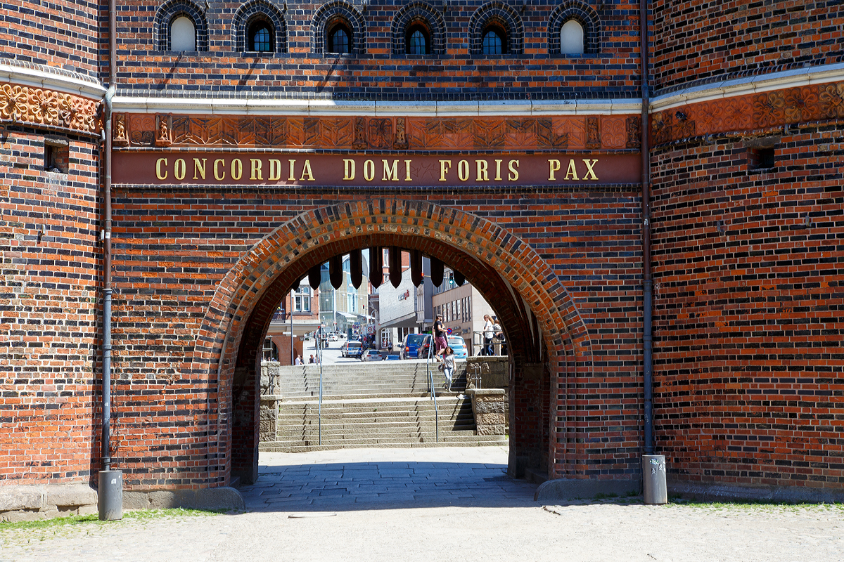 
Lübeck am 11.06.2015, Deteil vom Holstentor von Westen (Feldseite) mit der Innschift: 
Concordia domi foris pax („Eintracht innen, draußen Friede“). 

Dieser Schriftzug stammt von 1871 und ist eine verkürzte Form der Inschrift, die zuvor auf dem (nicht erhaltenen) Vortor gestanden hatte: Concordia domi et foris pax sane res est omnium pulcherrima („Eintracht innen und Friede draußen sind in der Tat für alle am besten“).

Obwohl mir die Übersetzung der heutigen Inschrift mit Google besser gefallen würde, hier würde es wie folgt übersetzt: Eintracht und Frieden im In- und Ausland (spricht auf der Welt)
