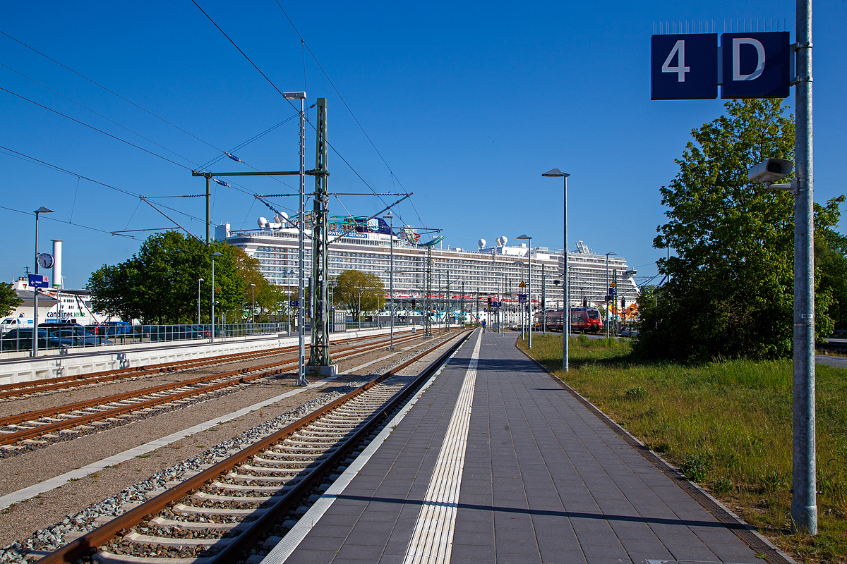 Mehr Schiffs- als Bahnbild...
Der Bahnhof Warnem�nde am 15.05.2022, Blickrichtung Warnem�nder Passagierkai (Warnem�nde Cruise Center), wo gerade die Norwegian Getaway der Norwegian Cruise Line liegt, da wirkt rechts auf Gleis 2 der einfahrende „Hamster“ (Bombardier Talent 2) der S-Bahn Rostock winzig. 

Der Bahnhof Warnem�nde liegt im gleichnamigen Ostseebad, einem Ortsteil der Hansestadt Rostock. Er ist Endpunkt der Linien S1, S2 und S3 der S-Bahn Rostock. Neben dem Rostocker Hauptbahnhof ist er der zweite Fernverkehrsbahnhof Rostocks mit IC Verbindungen nach Dresden, Wien und Leipzig. Bis 1995 war er Ausgangspunkt der F�hren nach Gedser in D�nemark (die zwei F�hrbetten wurden J2014/2015 durch eine neue Uferbefestigung �berbaut und dadurch beseitigt). Das Empfangsgeb�ude und einige weitere Anlagen des Bahnhofs stehen unter Denkmalschutz.

Die m�chtige Norwegian Getaway der Norwegian Cruise Line wurde von der MEYER WERFT GmbH in Papenburg (Deutschland) unter der Baunummer S.692 gebaut. Die Kiellegung war 30. Oktober 2012, der Stapellauf am 2. November 2013, die Taufe 7. Februar 2014 und am 10. Januar 2014 erfolgte die �bernahme durch die Reederei Norwegian Cruise Line. Das Schifft f�hrt unter der Flagge von den Bahamas.

Weitere Daten und Fakten der Norwegian Getaway:
Tonnage: 145.655 BRT
L�nge: 326 Meter
Breite: 52 Meter
Max Geschwindigkeit: 23 Knoten (42,5 km/h)
Anzahl Decks: 14
Passagiere: 3.963
Crewmitglieder: 1.646
Restaurants: 16
Maschinenleistung: 62.400 kW (84.840 PS) durch 4 � MAN-Dieselgeneratoren (Dieselelektrischer Antrieb
Propeller: 2 � Azipod (Propellergondel, auch Pod-Antrieb genannt)

Einfach ein riesiger Pott, da bleiben wir lieben auf den Schienen und machen eher eine Schienen-Kreuzfahrt. 

