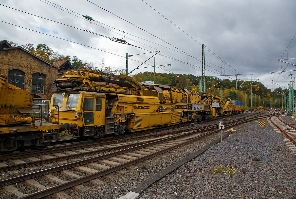 Plasser & Theurer Bettungsreinigungsmaschine RM 95-700
Die Plasser & Theurer Hochleistungs-Bettungsreinigungsmaschine RM 95-700, Schweres Nebenfahrzeug Nr. 99 80 9214 004-0 D-MGWB, ex 97 11 41 501 17-3, der MGW Gleis- und Weichenbau-Gesellschaft mbH & Co. KG (Berlin) am 22.10.2021 im Zugverband in Betzdorf (Sieg) bei einer Zugdurchfahrt.
 
Die Maschine wurde 2003 von Plasser & Theurer unter der Fabriknummer 4068 gebaut.

TECHNISCHE DATEN:
Bauart: RM 95-700
Spurweite: 1.435 mm (Normalspur)
Achsfolge:Bo´+Bo´Bo´+2´
Achsanzahl:  8
Länge: 48.240 mm
Drehzapfenabstände: 18.300 / 22.040 mm
Achsabstand im Drehgestell: 1.800 m	
Raddurchmesser: 920 mm (neu)
Höhe:  4.300 mm
Breite: 3.150 mm
Eigengewicht: 170,0 t
Motorengesamtleistung: 700 kW
V-Max Eigenfahrt:   20 Km/h
V-Max Zugverband: 100 Km/h
Zugkraft am Zughaken im Arbeitsbetrieb: ca. 300 kN
Streckenklasse: 	D4
zur Mitfahrt zugel. Personen: 4
Anhängelasten (Eigenfahrt):  40 t 
Anhängelasten (Arbeitsfahrt bei 10 ‰ Steigung):  1.000 t
Bremsarten: KE G – P mZK und D2b 
Handbremsgewicht: 30 t 
Kleinster befahrbarer Radius: 120 m

Besondere Ausstattung:
•Laser-Anlage zur genauen Steuerung der Reinigungstiefe bei Ablage des Gleises in Hochlage
•Reinigungsbreite von 3.800 mm bis 5.000 mm durch Ergänzungsbalken
•maximale Veschiebung Gleisrost +/- 30 cm
•Leistung bis zu 700 m³/h
•Dokumentation der Lage des Gleises hinter der Reinigungsmaschine durch MKS-Messschrieb  
•Automatisches Warnsystem für Maschinenwarnung (AWS)
•Neuschotterzuführung zur optimalen Verfüllung des gereinigten Gleises mit Schotter

RM 95-700 - Bettungsreinigung mit Doppelsiebanlage
Die RM 95-700 ist eine achtachsige, vollhydraulische Hochleistungsbettungsreinigungsmaschine mit Neuschotterzuführung in Gelenkbauweise, für den Einsatz auf dem Gleisnetz der DB AG. Der Antriebs- und Siebwagen fährt vorne auf einem zweiachsigen und hinten auf vierachsigem Triebdrehgestell (2x2 Doppeldrehgestell). Der Aushub- und Einschotterteil ist vorne am Antriebswagen angelenkt und fährt hinten auf einem Laufdrehgestell.

Materialaushub
Die Aushubkette ist eine Weiterentwicklung der weltweit bewährten Ketten von Plasser&Theurer und wurde hinsichtlich der Lebensdauer weiter optimiert. Sie ist als endlose Fünfecks-Kratzerkette mit einer Höhe von 300 mm ausgeführt. Die Kettengeschwindigkeit ist stufenlos im Bereich von ca. 1,8 bis 3,5 m/sec verstellbar, die maximale Räumtiefe beträgt 1.000 mm unter SOK der überhöhten Schiene. Die Maschine ist mit einem Räumbalken für eine Reinigungsbreite von 4 Meter ausgestattet. Für geringere Räumbreiten wird ein Kettenquerbalken mit 3,4 m geliefert. Der hydraulische Kettenquerbalkenverschluss vereinfacht den Einbau des Querbalkens und verringert wesentlich die erforderlichen Rüstzeiten. Im Bereich der Räumkette ist die kontinuierlich arbeitende Gleishebe- und Rückeinrichtung angeordnet. Die maximale Hebung beträgt 250 mm, die maximale seitliche Gleisverschiebung ± 300 mm.

Siebanlage
Die Maschine ist mit zwei robusten Schwingsieben mit einer Gesamtfläche von über 40 m2 ausgestattet, die für höchste Qualität und Leistung sorgen. In der Überhöhung in Bögen verstellt der Maschinist die Querneigung der Siebanlage hydraulisch um bis zu 160 mm, sodass die Siebe immer waagrecht bleiben. Der Abraum gelangt über Förderbänder zur Maschinenfront. Das Übergabeförderband ist drehbar ausgeführt, sodass kein Schutzwaggon für Überstellfahrten notwendig ist. Der Abraum kann seitlich neben dem Gleis, auf am Parallelgleis stehende Waggons oder auf ein von der Maschine geschobenes Abraumverladesystem abgeladen werden.

Schotterverteileinrichtung
Der gereinigte Schotter gelangt von der Siebeinrichtung über Förderbänder in einen Schotterspeicher und von hier aus über ein Bodenförderband, einen Schotterschacht und ein Einschotterungsband direkt hinter der Räumkette in den Gleisbereich. Der Schotterspeicher und die Förderbänder auf der Aushubmaschine ermöglichen einen Mengenausgleich bei Arbeitsbeginn und Arbeitsende. Der Einschotterpflug mit verstellbaren Pflugschildern sorgt für eine gleichmäßige Verteilung des gereinigten Schotters.

Neuschotteranlage
Mit der RM 95-700 ist die Zuführung von Neuschotter im Zuge der Bettungsreinigung möglich. Dazu wird der Neuschotter von den hinten angereihten Materialförder- und Siloeinheiten in den Zuführungsschacht gefördert, und über die verstellbaren Einschotterhosen die Stopfzonen gezielt eingeschottert.

Lasereinrichtung, elektronischer Schreiber
Die präzise Führung der Räumkette in Längs- und Querrichtung ist von entscheidender Bedeutung für die Arbeitsqualität bei der Bettungsreinigung. Daher wird mit einer Lasereinrichtung die Bezugsbasis für die Steuerung von Räumtiefe und Kettenquerneigung vergrößert, um einen noch präziseren Schnitt zu gewährleisten. Diese Lasereinrichtung besteht aus einem Lasersender, der in einer Entfernung von bis zu 300 m (abhängig von Gleisgeometrie und Sichtverhältnissen) aufgestellt wird, und einem Laserempfänger an der Maschine. Der Empfänger wird entsprechend der Wahl des Bezugsstranges links oder rechts auf Konsolen an der Kettenführung positioniert. Die Voreinstellung der Räumtiefe erfolgt durch den Maschinisten von der Arbeitskabine aus. Hier steht auch eine Anzeige für Räumtiefe und ein Zeigerinstrument für die Planumsneigung zur Verfügung. Weiter ist die Maschine mit einem digitalen Vierkanal-Schreiber ausgestattet, womit folgende Parameter aufgezeichnet werden:
Räumtiefe
Planumsneigung
Überhöhung des gereinigten Gleises 
Verwindung des gereinigten Gleises

Kabinen
Alle Kabinen sind geschlossen, schallisoliert und vibrationsgedämpft ausgeführt. Gute Sichtverhältnisse sind gewährleistet. Kabinenheizung, Kabinenlüfter mit Luftfilter sowie Klimaanlagen (optional) sorgen für komfortable Bedingungen bei unterschiedlichen klimatischen Bedingungen während des Arbeitseinsatzes. In allen Kabinen ist außerdem eine Wechselsprechanlage installiert. Vorne und hinten befindet sich jeweils eine Fahrkabine mit den Bedienungselementen für Rangierfahrten. Direkt vor der Räumkette befindet sich die Arbeitskabine. Sie enthält sämtliche Bedienungselemente für die Kette, Hebe- und Rückeinrichtung, Arbeitsvorschub etc.

Die RM 95-700 ist eine Maschine für viele Einsatzmöglichkeiten
Mit der RM 95-700 steht eine Maschine zur Verfügung, die aufgrund ihres Konzeptes bei unterschiedlichen Baustellensituationen flexibel eingesetzt werden kann. Die RM 95-700 bietet dabei eine Reihe von Vorteilen:
•Hohe Arbeitsleistung durch die hohe Siebleistung
•Präziser Planumsschnitt durch Lasersteuerung
•Integrierte Neuschotterzuführung, damit ausreichender Schotter auch für die Ein- und Ausbaustelle und somit eine besser Nutzung der Sperrpausen
•Kurze Materialtransportwege innerhalb der Maschine
•Schotterspeicher für Materialmengenausgleich bei Baustellenanfang und Baustellenende
•Kurze Rüstzeiten durch hydraulischen Kettenquerbalkenverschluss und Montagekran
•Hohe Zugkraft durch drei angetriebene Drehgestelle
•Robuste Konstruktion des Maschinenrahmen
•Leistungsfähige Räumkette


Quelle: MGW Gleis- und Weichenbau-Gesellschaft mbH & Co. KG 
