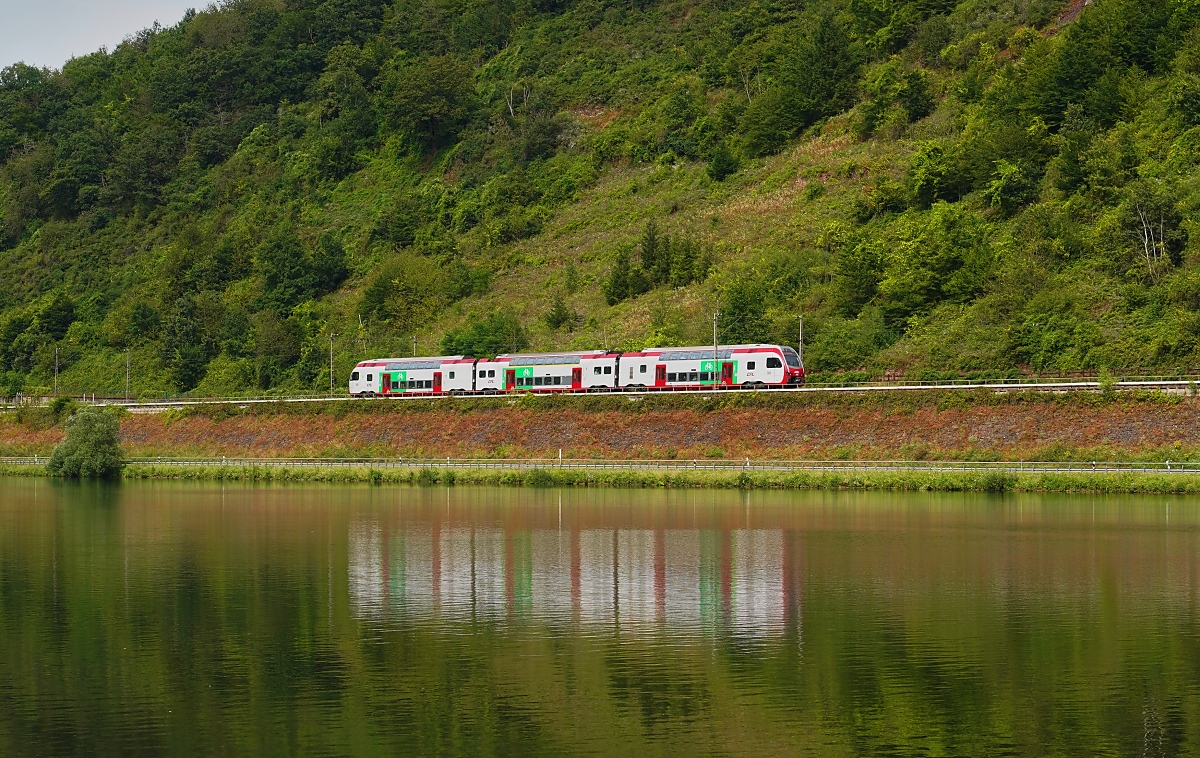 Seit einigen Jahren besteht eine tägliche Direktverbindung Luxemburg - Düsseldorf und zurück, die mit Stadler Kiss der CFL bedient wird. Dieser Zug wird zwischen Koblenz und Düsseldorf als IC geführt, während er auf der übrigen Strecke als RE 1 unterwegs ist und damit für den Regionalverkehr freigegeben ist. Am 25.07.2024 fährt der IC/RE 1 5106 bei St. Aldegund entlang der Mosel in Richtung Luxemburg.