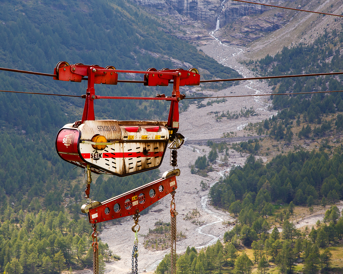 Unterhalb Alp Grüm werden die Alp Grüm der Berninabahn erneuert, daher gibt es eine Materialseilbahn von Alp Grüm hinab zu den Galerien, hier am 06.09.2021. So wird oben in Alp Grüm der Beton gemischt und dann mit der Seilbahn hinab gefahren. 

Die hier verwendete Bahn ist vom italienischen Seilbringungs-Spezialisten Seik (Truden). Der verwendete Wagen ist ein Seilkran vom Typ SFM 30/60.  In dem Seilkran befindet sich ein Verbrennungsmotor der das Hubwerk antreibt (dieser läuft nur bei der Hubbewegen) um wie hier den Betonkübel anzuheben und später wieder abzusenken. Die Hubkraft beträgt im Einzelzug 3t oder wie hier im Doppelzug mit dem Waagbalken 6t. Das Gesamtgewicht beträgt ca. 1t. Die Winde für das Zugseil kann nach Belieben (Bergseite – Talseite) platziert werden.