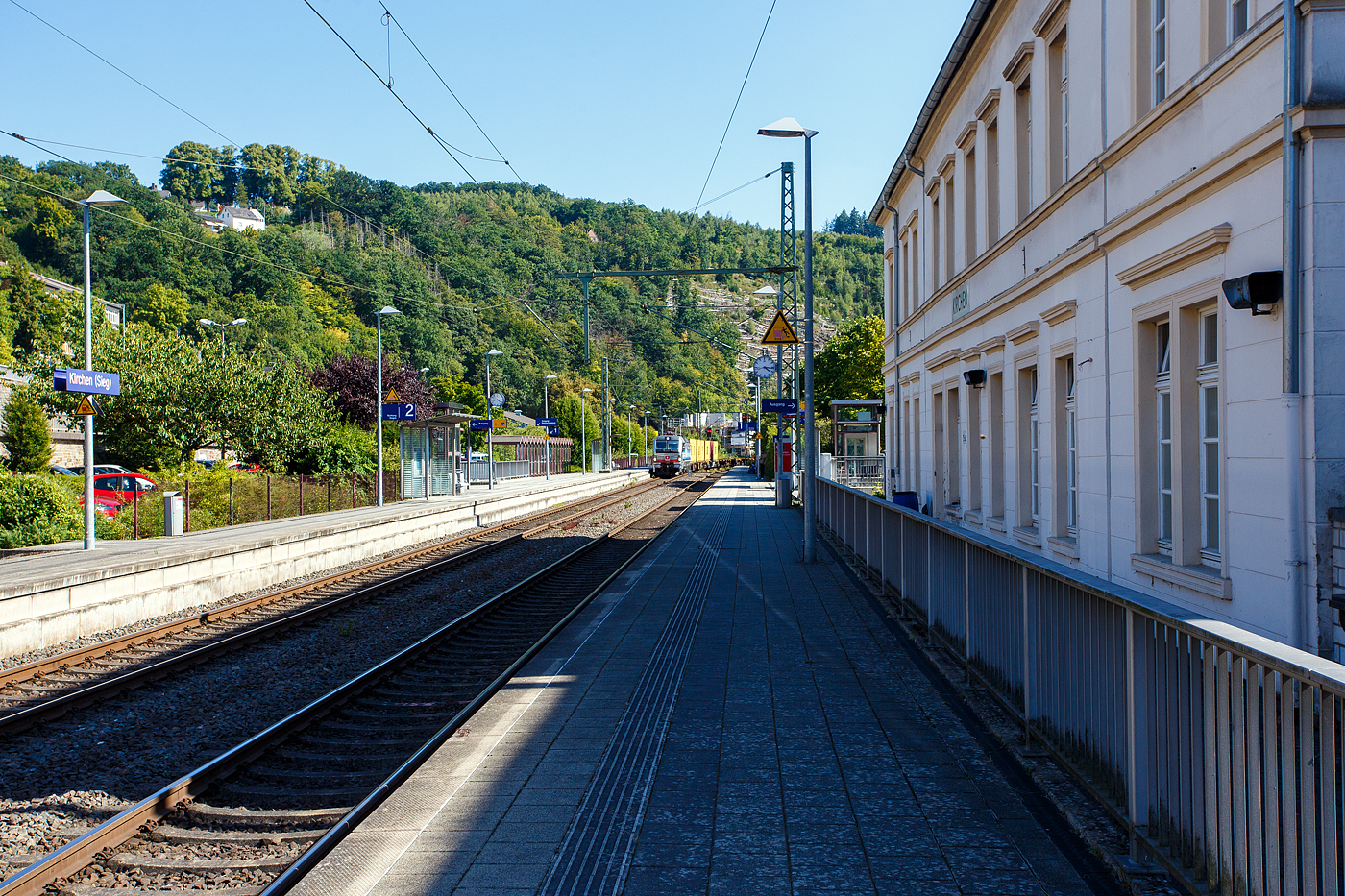 Der Bahnhof Kirchen/Sieg bei km 120,7 an der Siegstrecke (KBS 460) am 18 August 2025 in Blickrichtung Betzdorf. Hinten kommt die an die SBB Cargo International AG vermietete Siemens Vectron MS - 193 110  Zugersee  (91 80 6193 110-4 D-Rpool) der Railpool GmbH (München), mit einem Containerzug.