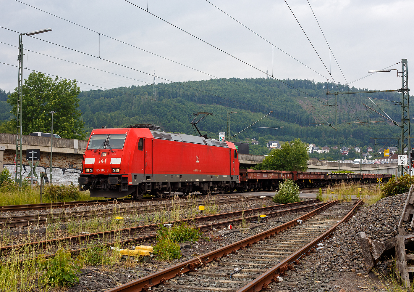 Die 185 306-8 (91 80 6185 306-8 D-DB) der DB Cargo AG fährt am 10 Juni 2025, mit einem leeren Coilzug (sechsachsige Wagen u.a. der Gattung Sahmms 711.0), durch Niederschelden und Niederschelderhütte in Richtung Köln. Die Lok hat hier gerade die Sieg überquert und somit auch die Landesgrenze zwischen Nordrhein-Westfalen und Rheinland-Pfalz. 

Die TRAXX F140 AC2 wurde 2007 von der Bombardier Transportation GmbH in Kassel unter der Fabriknummer 34174 gebaut und an die DB Cargo AG (damals Railion Deutschland AG) geliefert.