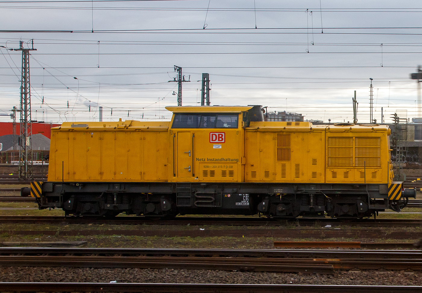 Die 203 315-7 (92 80 1203 315-7 D-DB) der DB Netz AG steht am 21.03.2023 bei Frankfurt am Main (aus einem Zug heraus fotografiert).

Die V 100.1 wurde 1973 bei LEW (VEB Lokomotivbau Elektrotechnische Werke „Hans Beimler“, Hennigsdorf) unter der Fabriknummer 13943 gebaut und als 110 625-1an die DR ausgeliefert.

Weiterer Lebenslauf:
1983  Umbau Bw Karl-Marx-Stadt  in DR 112 625-9
01.01.1992 Umzeichnung in DR 202 625-0
01.01.1994 DB  202 625-0
2002  an ALS - ALSTOM Lokomotiven Service GmbH (Stendal) hier erhielt sie einen neuen CAT-Motor und wurde entsprechend in 203 315-7 umbezeichnet.
2003  an DB Bahnbau GmbH
Und seit 2004 bei der DB Netz AG