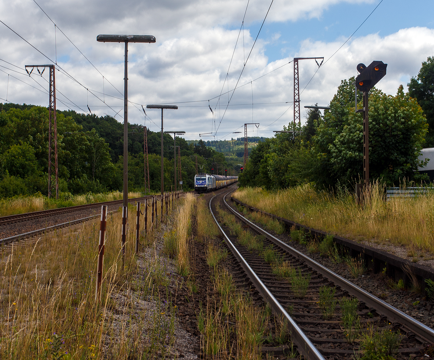 Die an die RTB Cargo (RATH Gruppe/Rurtalbahn) vermietete Railpool 186 297-8 (91 80 6186 297-8 D-Rpool), fährt am 11 Juli 2025 mit einer weiteren kalten 185 oder 186er und mit einem langen geschlossen Doppelstock- Autotransportzug der ARS Altmann AG (mit Wagen der Gattung Hccrrs), durch Rudersdorf (Kreis Siegen) in Richtung Siegen bzw. Köln.
