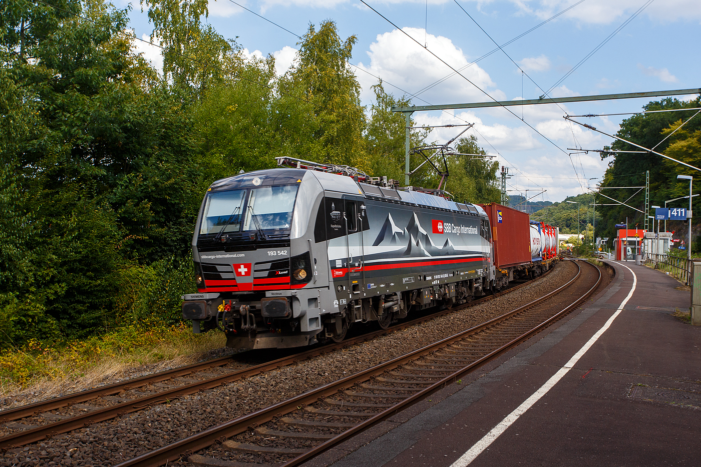 Die an die SBB Cargo International AG vermietete mit XLoad ausgestattete SIEMENS Vectron 193 542  Kapellbrücke Luzern  (91 80 6193 542-8 D-SIEAG) der SüdLeasing GmbH, Stuttgart (eingestellt in Deutschland durch Siemens) fährt am 21
 August 2025, mit einem KLV-Zug, durch Scheuerfeld/Sieg in Richtung Köln.

Die Multisystemlokomotive Siemens Vectron MS wurde 2024 von Siemens Mobilitiy in München-Allach unter der Fabriknummer 23559 gebaut und am 19.09.2024 ausgeliefert. Sie wurde in der Variante A40-1a ausgeführt und hat so die Zulassung für Deutschland, Österreich, die Schweiz, Italien, die Niederlande und Belgien (D / A / CH / I / NL / B). Sie verfügt über eine Leistung von 6,4 MW (160 km/h) und ist neben den nationalen Zugsicherungssystemen mit dem Europäischen Zugsicherungssystem (ETCS BL3) ausgestattet. Zudem ist sie mit der neuen Ausrüstungspaket XLoad ausgestattet.

Das neue XLoad Ausrüstungspaket für Vectron:
XLoad ist ein Ausrüstungspaket für Vectron, welches künftig mitbestellt, aber auch bei bereits ausgelieferten Vectron Loks nachgerüstet werden kann. Das Feature verbessert die Reibwertausnutzung und ermöglicht dadurch höhere Anhängelasten. Zudem reduzieren die Fahreigenschaften, die das Feature bewirken, den Verschleiß von Rad und Schiene.

Aktuell sind die Schweizer Vectron-Lokomotiven (SBB Cargo und BLS Cargo) in der Regel in Doppeltraktion unterwegs. Die Steigungen und Rampen der Schweizer Berge sind vor allem bei schlechten Witterungsbedingungen nicht ohne. Eine Lokomotive muss auch bei geringerem Schlupf genügend Traktion auf die Schienen bringen, um alle Güter sicher und zuverlässig ans Ziel zu bringen. Ein effizienter Weg aus dieser «Misere» ist die für Vectron entwickelte Zusatz-Funktion «XLoad». Den erfolgreichen Beweis trat eine SIEMENS Testlokomotive im Frühjahr 2022 bei der SBB Cargo International und bei der BLS Cargo eindrücklich an.

Für SBB Cargo International bewies die Test-Lokomotive am Bözberg und für BLS Cargo an der Nordrampe des Lötschbergs ihre enorme Zugkraft.
Vectron meisterte im Frühjahr 2022 die lange 12‰-Steigung des Bözbergs mit einer Anhängerlast von 2.000 Tonnen bravourös. Bei den nächtlichen Testfahrten zeigte sich eindrücklich die enorme Zugkraft der Lokomotive.

Am Lötschberg wurden bei der BLS Cargo steigungsmäßig noch ein paar Promille draufgepackt. Mit 1.020 Tonnen im Gepäck bewältigte die Vectron-Lokomotive mit XLoad-Feature die 27‰-Steigung der Nordrampe ebenfalls meisterlich. Und auch diverse Anfahrtsversuche absolvierte der mit dem XLoad-Feature aufgerüstete Vectron problemlos.

So bestellte die SüdLeasing GmbH (Stuttgart) im Auftrag der SBB Cargo International jüngst 20 Vectron Lokomotiven mit XLoad bei SIEMENS.