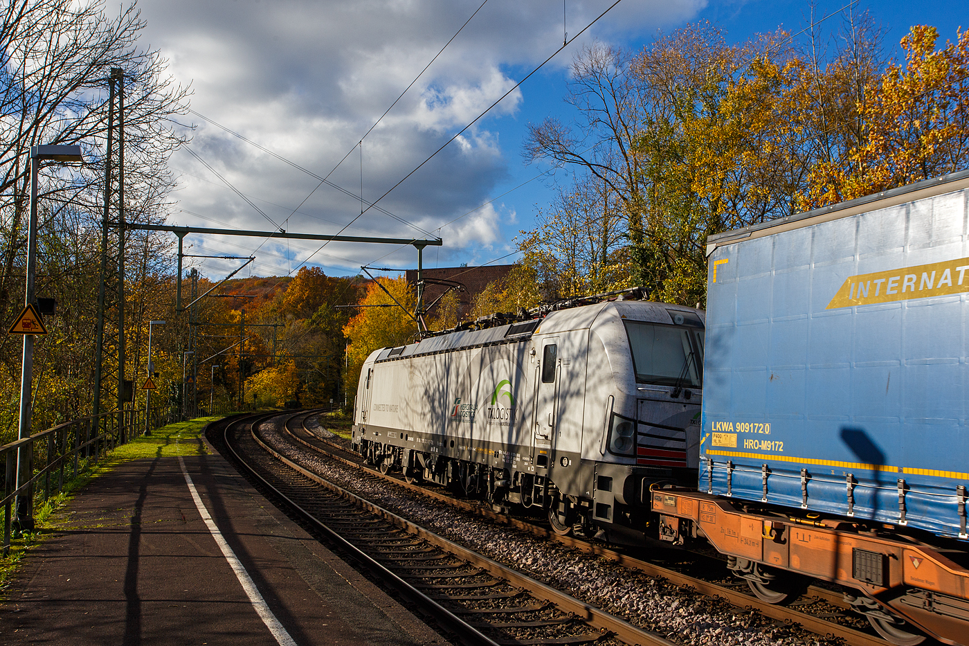 Die recht neue wei�e TXL 7193 318 „Connected to Nature“ (91 80 7193 318-1 D-TXL) der TXL - TX Logistik AG (Troisdorf) f�hrt am 30 Oktober 2025 mit einem KLV-Zug durch Scheuerfeld/Sieg in Richtung K�ln. Als Schlussl�ufer war am Zugschluss zudem die kalte, an die HSL Logistik GmbH vermietete, AKIEM 186 383-6.

Nochmals einen lieben Gru� an den netten Lokf�hrer zur�ck.

Die SIEMENS Vectron MS (X4E) wurde 2024 von Siemens Mobility in M�nchen-Allach unter der Fabriknummer 24282 gebaut und am 24.01.2025 an die TXL ausgeliefert. Die mit 6.400 kW konzipierte Mehrsystemlok ist in der Variante A22-11i ausgef�hrt und hat so die und hat so die Zulassungen und entspr. L�nderpakete f�r Deutschland, �sterreich, Schweiz, Italien und die Niederlande (D / A / CH / I / NL).

�ber TX Logistik AG
TX Logistik wurde 1999 als privates Eisenbahnverkehrsunternehmen gegr�ndet und bietet mit Verbindungen in elf L�ndern ein leistungsf�higes europ�isches Netzwerk. Das Unternehmen verf�gt �ber Tochtergesellschaften in der Schweiz, �sterreich, D�nemark und Schweden sowie eine lokale Pr�senz in Italien. In den Gesch�ftsbereichen Intermodal und Rail Freight entwickelt TX Logistik umfassende Schienenl�sungen f�r kontinentale und maritime Verkehre sowie ma�geschneiderte Konzepte f�r konventionelle Fracht. Mit 650 Mitarbeitern und 8,6 Milliarden gefahrenen Tonnenkilometern erwirtschaftete das Unternehmen 2021 einen Jahresumsatz von 253 Millionen Euro. Seit Januar 2017 geh�rt TX Logistik zu 100 Prozent der Mercitalia Logistics S.p.A., einer Tochtergesellschaft der FS - Ferrovie dello Stato Italiane. Mittlerweile geh�rt das Unternehmen mit zu den Gr��ten f�r den Schieneng�terverkehr in Europa.

Das Unternehmen bietet den ganzen Umfang an Schieneng�terverkehr, inklusive Containertransport und kombiniertem Verkehr an. Wichtigste Transportstrecken sind von den H�fen Hamburg, Bremerhaven, Rotterdam und Antwerpen nach S�ddeutschland, Schweiz, �sterreich und Italien.

TX Logistik setzt nun auf eigene Vectron Loks:
Anfang Oktober 2024 hat die TX Logistik AG ersten drei von 40 modernen Vectron-Lokomotiven des Herstellers Siemens Mobility aufs Gleis gesetzt, die das zur Mercitalia Logistics (FS Italiane Group) geh�rende Schienenlogistikunternehmen im Mai 2023 bestellt hatte. Die Erweiterung der Fahrzeugflotte ist f�r TX Logistik eine wichtige Voraussetzung, um im intermodalen und grenz�berschreitenden Schieneng�terverkehr weiter zu wachsen. Die neuen Lokomotiven werden vor allem auf dem Brenner- und dem Schweiz-Korridor eingesetzt, den strategisch wichtigen Nord-S�d-Achsen in Europa.

Beide Korridore sind stark frequentiert und stellen hohe Anforderungen an die eingesetzten Lokomotiven – von der Zugkraft �ber die Stabilit�t bis hin zur grenz�berschreitenden Systemkompatibilit�t. TX Logistik hat dazu die Maschinen mit verschiedenen L�nderpaketen bestellt. 20 Vectron erhalten das L�nderpaket f�r den Betrieb in Deutschland, �sterreich, Schweiz, Italien und den Niederlanden (D-A-CH-I-NL) und sollen bis Anfang 2025 �bergeben werden. Die Auslieferung der 20 Lokomotiven mit der Ausstattung f�r den deutsch-�sterreichisch-italienischen Korridor (D-A-I) soll bis zum Jahresende 2025 erfolgen.

Die Entscheidung f�r den Kauf der Vectron-Lokomotiven unterstreicht zugleich das Bestreben von TX Logistik, Schieneng�terverkehre als umweltfreundliche und effiziente Alternative zum Stra�entransport weiter voranzutreiben. Um dies zu unterstreichen und gleichzeitig f�r den Einstieg in den intermodalen Transport zu werben, hat die erste der drei Vectrons, die im Zughotel in Braunschweig �bergeben wurden, eine spezielle Lok-Beklebung mit dem Schriftzug „Start now (Nature). Driven by Green Passion“ erhalten.

Die neuen Loks bieten mit ihrer Flexibilit�t und Leistungsf�higkeit ideale technische Voraussetzungen, um den steigenden Anforderungen des europ�ischen G�terverkehrs gerecht zu werden. Mit der modernen Vectron-Flotte, so TX Logistik, sei man mittelfristig nun in der Lage, die Kapazit�ten auf dem Brenner- und dem Schweiz-Korridor deutlich zu erh�hen sowie die Effizienz und Zuverl�ssigkeit im Schieneng�terverkehr weiter zu verbessern.
