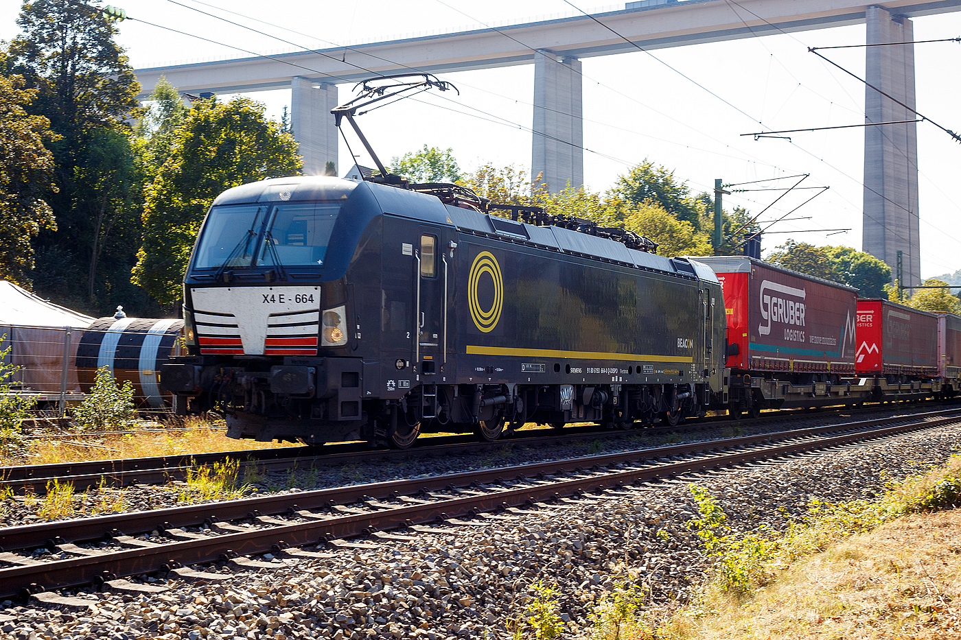 Die SIEMENS Vectron MS X4E – 664 / 193 664-0 (91 80 6193 664-0 D-DISPO) der BRCE - Beacon Rail Capital Europe (München) fährt am 21 September 2024 mit einem KLV-Zug durch Eiserfeld in Richtung Siegen. 

Die Multisystemlokomotive Siemens Vectron MS wurde 2017 von Siemens Mobilitiy in München-Allach unter der Fabriknummer 22244 gebaut. Sie wurde in der Variante A09 (Zulassungen für D / A / I) ausgeführt. Im Jahr 2022 erfolgte bie Siemens in München-Allach der Umbau in die Variante A22 und hat so die Zulassung für Deutschland, Österreich, die Schweiz, Italien und die Niederlande (D / A / CH / I / NL). So besitzt die Variante MS A22 folgende Zugsicherungssysteme: ETCS BaseLine 3, sowie für Deutschland (PZB90 / LZB80 (CIR-ELKE I)), für Österreich (ETCS Level 1 mit Euroloop, ETCS Level 2, PZB90 / LZB80), für die Schweiz (ETCS Level 2, ZUB262ct, INTEGRA), für Italien (SCMT) und die Niederlande (ETCS Level 1, ETCS Level 2, ATB-EGvv)

Die Lok wurde an die MRCE - Mitsui Rail Capital Europe GmbH in München ausgeliefert, seit September 2023 hat die Beacon Rail Metro Finance B.V. die Mitsui Rail Capital Europe B.V. (Amsterdam) und somit auch die Mitsui Rail Capital Europe GmbH im München übernommen, so firmiert sie nun als Beacon Rail Capital Europe GmbH, München (BRCE / DISPO).