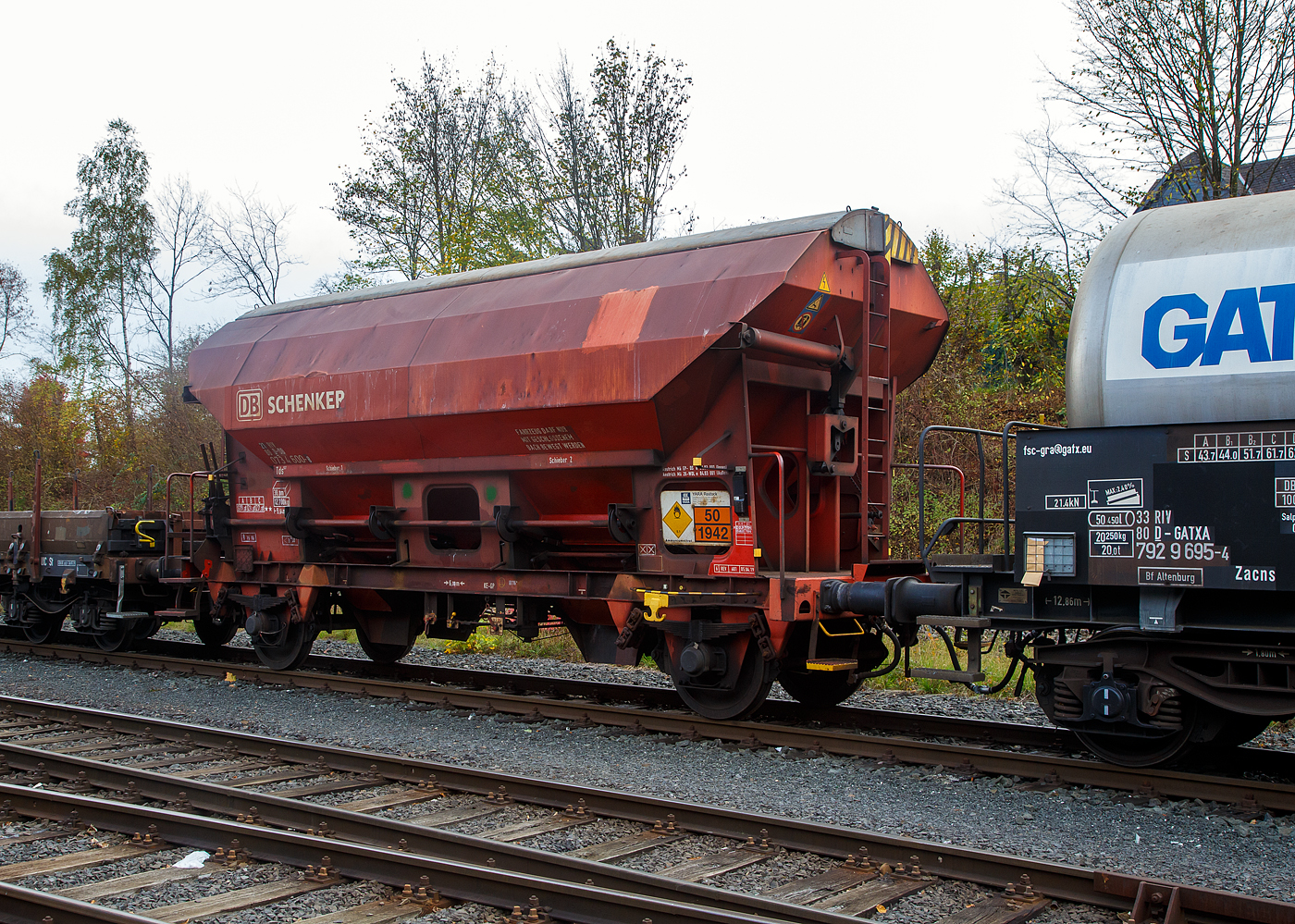 Gedeckter Schüttgutwagen mit dosierbarer Schwerkraftentladung und zwei Radsätzen 21 80 0734 600-8 D-DB, der Gattung Tds 937, der DB Cargo AG abgestellt, im Zugverband eines Übergabezuges der KSW, am 03.11.2022 in Herdorf auf dem Rbf. der KSW.

In diesen Wagen wird Ammoniumnitrat (Gefahrgutnummer 50/1942) zur Sprengstoff Herstellung zur Fa. Dynamit Nobel Defence nach Burbach-Würgendorf gefahren (hier ist er leer).  Ammoniumnitrat ist der Stoff  von dem ca. 2.750 Tonnen im Hafen von Beirut am 4. August 2020 explodierten und zur der bekannten gewaltigen Explosionskatastrophe führten.

Der Wagen trägt außerdem einen Aufkleber der Firma YARA Rostock, das zum norwegischen Konzern Yara International gehört. Yara ist ein Hersteller und Anbieter von Chemikalien und Industriegasen wie Dünger, Harnstoff, Nitraten und Ammoniak. Das Unternehmen entstand 2004 durch Abtrennung vom Unternehmen Hydro Agri, einem Firmenbereich von Norsk Hydro.

Die Wagen besitzen eine gleisseitige, dosierbare Entladeeinrichtung. Ein Innenanstrich erhöht bei den meisten der Fahrzeuge den Gebrauchswert, insbesondere durch den Schutz vor Verunreinigungen, Möglichkeiten des Transportes von Lebensmitteln, günstigeres Entladeverhalten (Rutschverhalten) bei schwer fließenden Gütern sowie durch verbesserten Korrosionsschutz bei aggressiven Ladegütern.

Der Wagen ist für den Transport von nässeempfindlichen Schüttgütern aller Art, wie z. B. Salze und Düngemittel, vorgesehen. Sie besitzen eine gleisseitige, dosierbare Entladeeinrichtung. Ein Innenanstrich erhöht bei den meisten der Fahrzeuge den Gebrauchswert, insbesondere durch den Schutz vor Verunreinigungen, Möglichkeiten des Transportes von Lebensmitteln, günstigeres Entladeverhalten (Rutschverhalten) bei schwer fließenden Gütern sowie durch verbesserten Korrosionsschutz bei aggressiven Ladegütern. Der Transport grobkörniger oder kantiger, schwerer Güter (z. B. Kies, Schlacke, Schotter) ist wegen einer möglichen Beschädigung der Innenbeschichtung nicht zulässig.

Das Untergestell und der Wagenkasten sind als Schweißkonstruktion unter Verwendung von Walzprofilen und Blechen hergestellt. Beide Teile sind miteinander verschweißt. Der Wagen besitzt zwei Bühnen, die von beiden Seiten zugänglich sind. Beide Bühnen sind mit einer Sprossenleiter versehen. Die Arbeitsbühne ist mit Handhebeln zur Betätigung der Wölbschieber, mit dem Handrad zur Öffnung des Daches und teilweise mit einer Feststellbremse und Notbremshahn ausgerüstet. Der Neigungsgrad des trichterförmigen Wagenkastens ermöglicht eine restlose selbsttätige Entladung. Die Entladung des Wagens erfolgt über Wölbschieber. Der Wagen ist mit einem einschaligen Hubschwenkdach ausgerüstet. Das Dach wird vor dem Schwenken angehoben und dann seitlich abgeschwenkt, wobei die gesamte Breite der Beladeöffnung freigegeben wird. Im geschlossenen Zustand ist das Dach gegen unbeabsichtigtes Verschwenken gesichert.

TECHNISCHE DATEN:
Spurweite: 1.435 mm
Achsanzahl: 2
Länge über Puffer: 9.640 mm
Achsabstand: 6.000 mm
Laufraddurchmesser: 1.000 mm (neu)
Wagenhöhe: 4.198mm
Größe der Beladeöffnung Länge x Breite: 8.000 x 1.200 mm
Laderaum: 38 m³
Eigengewicht: 12.700 kg
Höchstgeschwindigkeit: 100 km/h (beladen) / 120 km/h (leer)
Maximales Ladegewicht: 27,0 t  ab Streckenklasse C
Kleinster bef. Gleisbogenradius: 35 m
Bauart der Bremse: KE-GP (LL)
Bremssohle: IB 116
Intern. Verwendungsfähigkeit: RIV

Auch in dem Kesselwagen davor 33 80 7929 695-4 D-GATXD, der Gattung Zacns, wurde ein Rohstoff für die Herstellung von Sprengstoffen transportiert und zwar Salpetersäure.