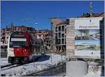 Der TPF ABe 2/4 102  SudExpress  verlässt den Bahnhof von Châtel St-Denis, während das Plakat rechts im Bild einen nicht ganz stimmigen Blick in nahe Zukunft erlaubt: Ein TPF RABe 526